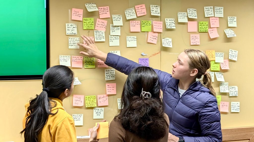 3 students standing in front of a board covering in dozens of sticky notes