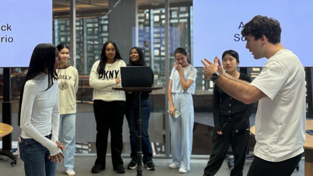 Sebastian Groundstroem acting out a scenario with a student during a presentation. Other students are standing watching in the background