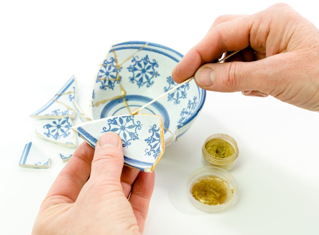 Hands mending a bowl with gold in the 'Kinstsugi' technique