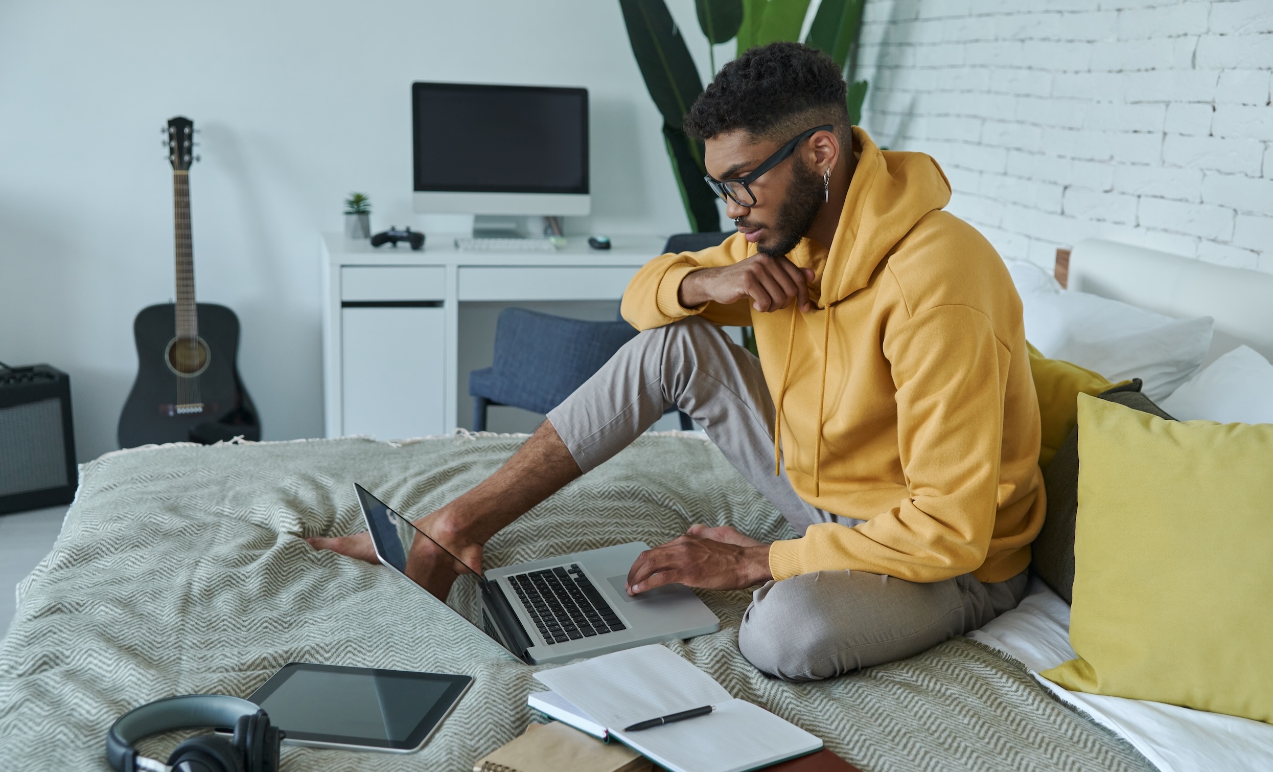 a man sitting on a bed, with laptop books and headphones