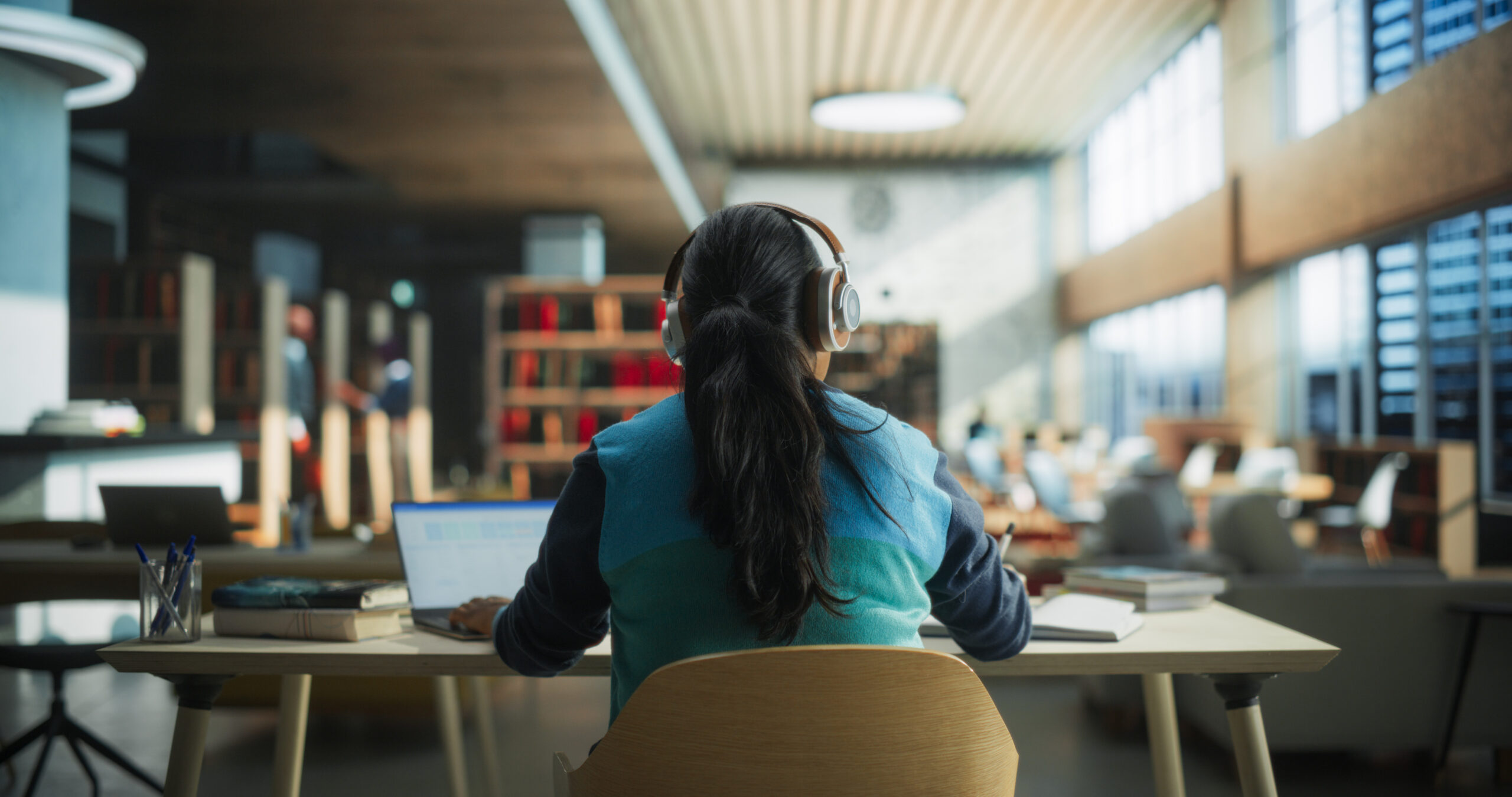 Female Student Wearing Headphones while Working in a Public Library.